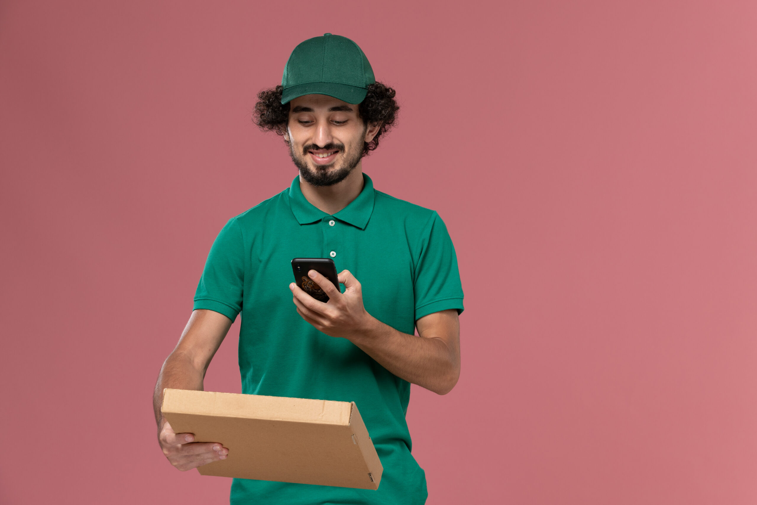 front view male courier green uniform cape holding delivery food box taking photo pink background service worker uniform delivery job